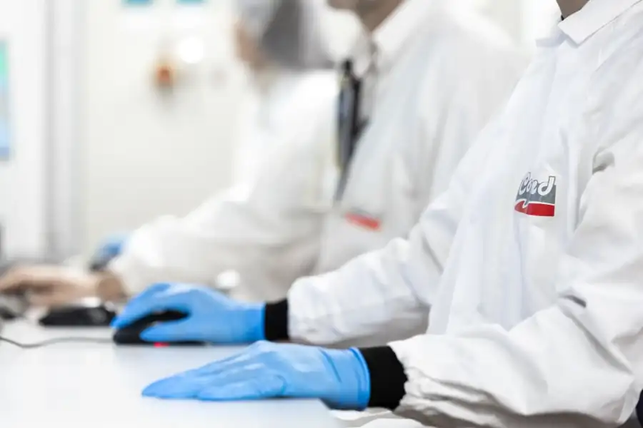 Operatori con guanti e camici monitorano la produzione tramite un computer