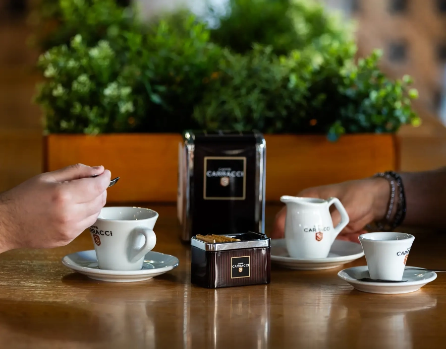 Tavolo del bar con tazzina di caffè, tazzina di cappuccino, lattiera, porta fazzoletti e porta zucchero marcati Carracci